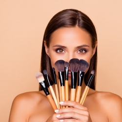 femme se cachant derrière des pinceaux de maquillage