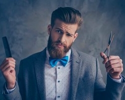 homme barbu en costard gris et noeud bleu tenant dans ses mains un peigne et un ciseau