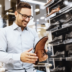 homme dans un magasin faisant du shopping qui sourit avec une chaussure dans ses mains